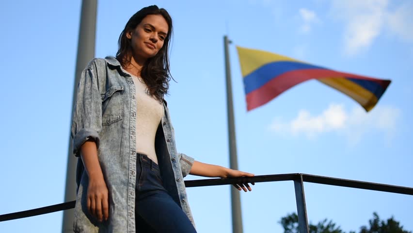 Proud happy woman in front of Colombian flag in Medellin, Beautiful young tourist woman smiling in front of the Colombian flag