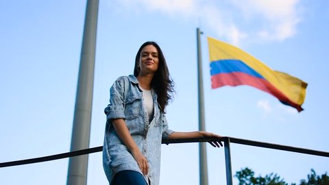 Beautiful young girl in front of Colombian flag in the wind, Smiling happy tourist posing in front of Colombian flag