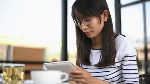 Beautiful young  Asian girl with tablet in cafe drinking coffee and working on tablet.