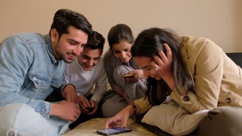 Friends seated in a circle and look at a touch screen mobile phone device as they share and discuss something in the bedroom