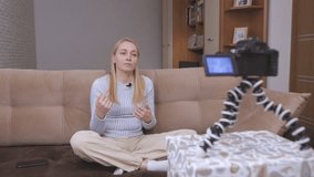 Woman videobloger shoots vlog in front of the camera while sitting on the couch
