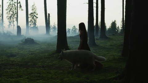 White dog and a girl walking in a forest.