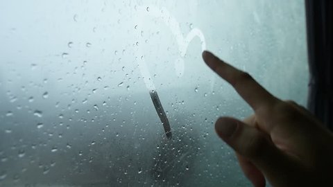 Woman finger draws a love heart symbol, on a wet rainy window.