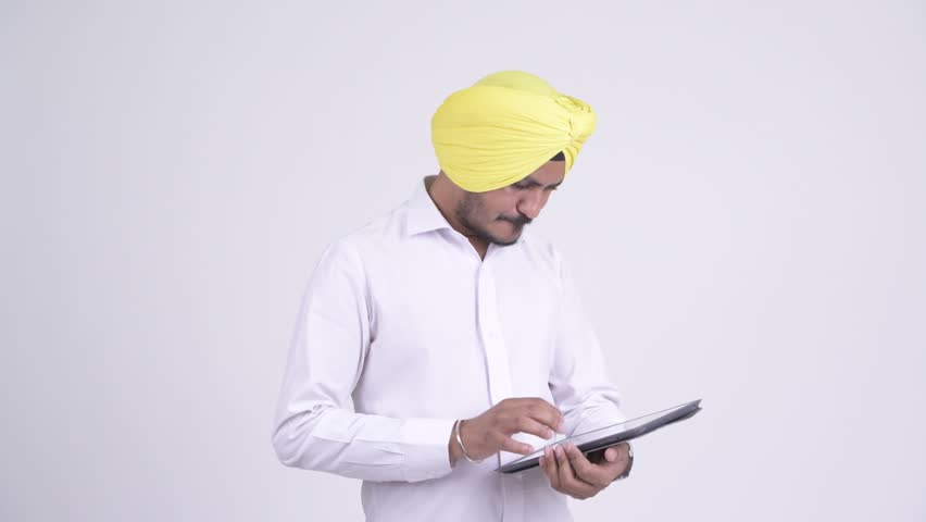 Stressed bearded Indian Sikh businessman using digital tablet and getting bad news