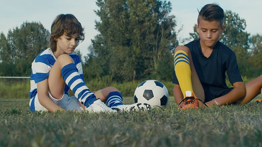 Young soccer players buckle their shoes before the training on a field, 4k slow motion