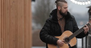 4k Footage of bearded man standing on the street and playing on his guitar with blurred background. - Video