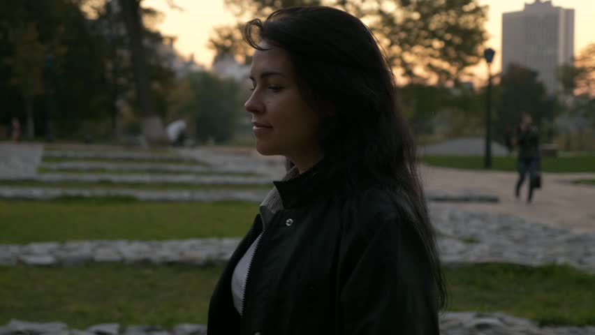 After Work Pretty Girl Walks In Dusk Park In The Evening. Autumn Evening City Background. 4K Slow motion 60 fps