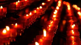 Burning red round candles in a catholic church. Female hand lights a candle