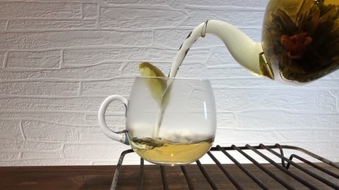 Hot tea is poured into a glass cup from an elegant transparent teapot and placed on an iron stand. 4K slow motion