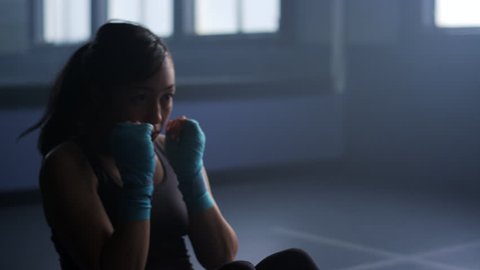 Close up of a sweaty, female boxer warming up with sit-up punches in an old, dimly lit boxing gym
