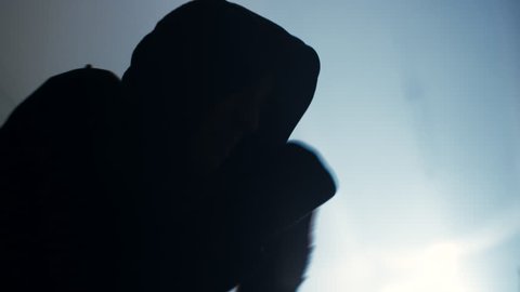 Close up of a hooded male athlete shadow boxing in a foggy, dimly lit room. He stops and looks intensely at the camera
