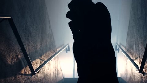 Close up of a silhouetted male fighter shadow boxing in a foggy, dimly lit stairwell