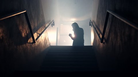 A hooded male boxer throws powerful punches, while training in a dark, hazy stairwell