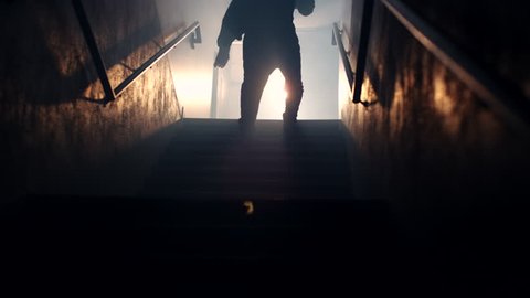 A hooded male athlete runs up a dark, hazy stairwell and shadowboxes intensely at the top