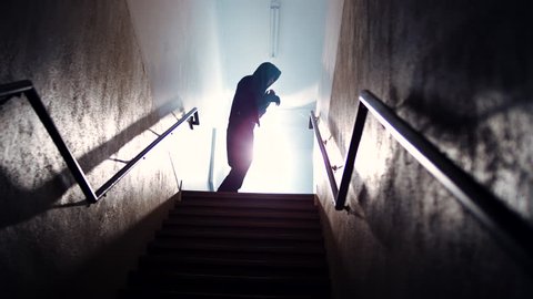 A hooded male athlete shadow boxes at the top of a dark, foggy stairwell