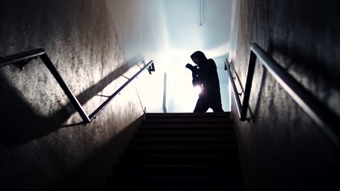 A hooded male boxer throws punches while shadow boxing at the top of a dark, foggy stairwell