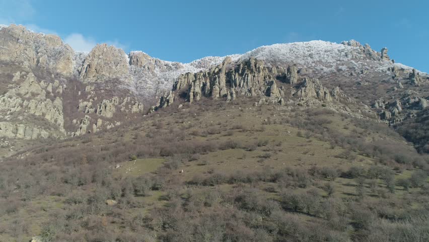 Majestic rock formation on a green mountainside covered by shrubs on a clear sunny day against the blue clear sky. Shot. Aerial view.