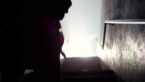 A hooded male boxer runs up a dark, foggy stairwell and shadow boxes towards the light
