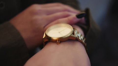 Woman with black nails checking time on gold watch