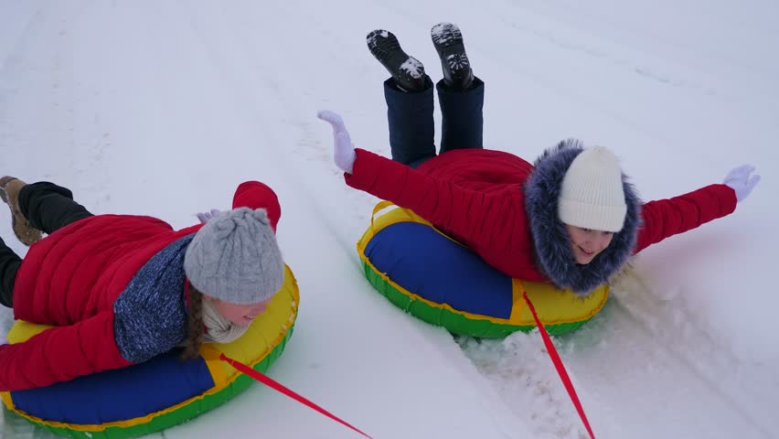 Happy teen girls go but snowy road in winter snowy mountain, straightening their arms in flight and laughing. Happy childhood in winter on sled. Christmas Holidays. | Shutterstock HD Video #1022523373