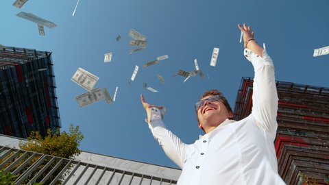 SLOW MOTION EFFECT, BOTTOM UP, CLOSE UP: Smiling Caucasian man celebrating winning the lottery by tossing money in the air. Businessman gets a lot of cash after successfully finishing work project.