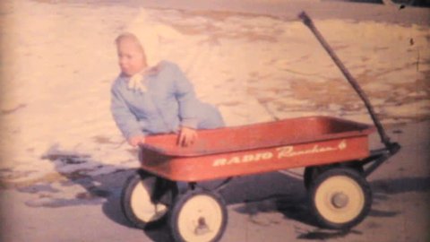 WALLA WALLA, WASHINGTON, 1964: A cute little girl has fun playing with her new red wagon outside in the snow in 1964.