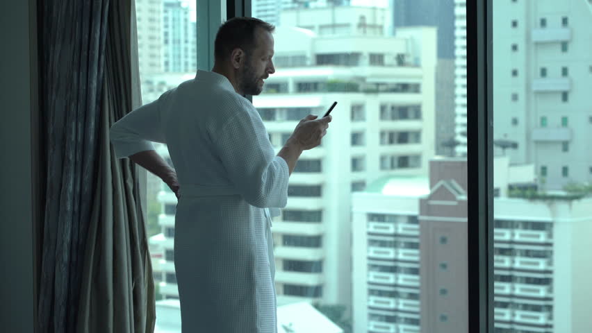 Man wearing bathrobe and texting messages on smartphone
