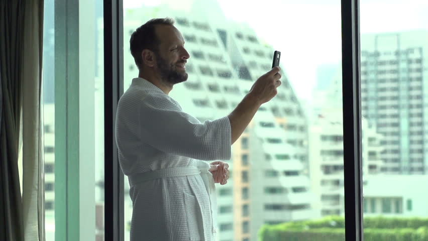 Happy man wearing bathrobe and doing selfies on smartphone, slow motion shot at 240fps
