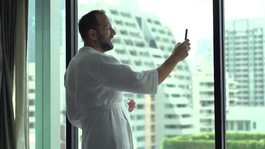 Happy man wearing bathrobe and doing selfies on smartphone, slow motion shot at 120fps
