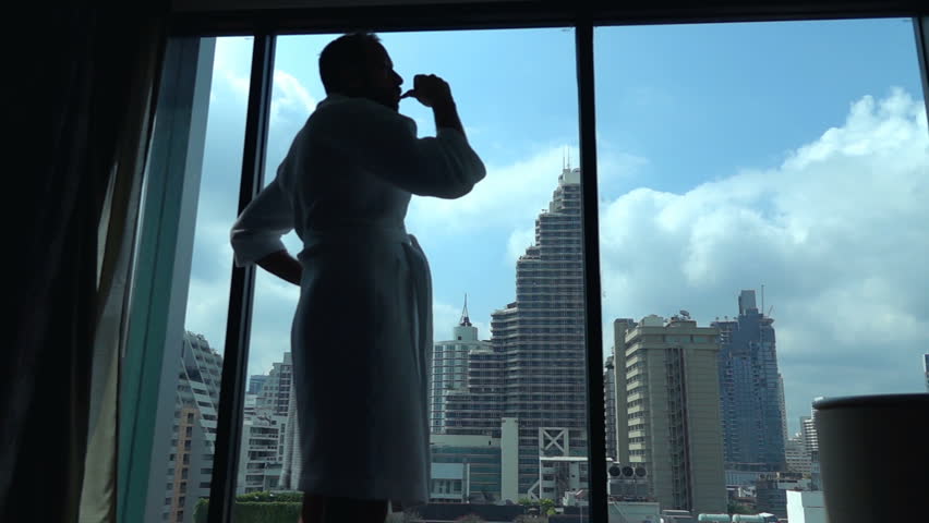 Man wearing bathrobe and brushing his teeth by the window, slow motion shot at 240fps 
