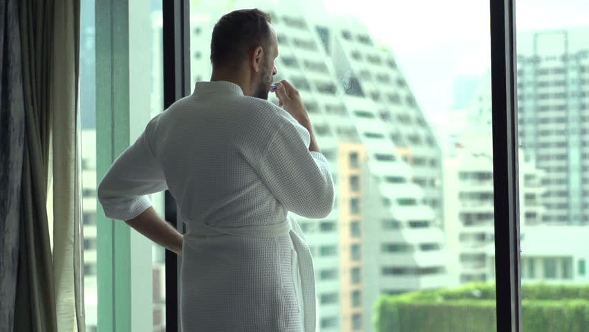 Man wearing bathrobe and brushing his teeth by the window, slow motion shot at 120fps 
