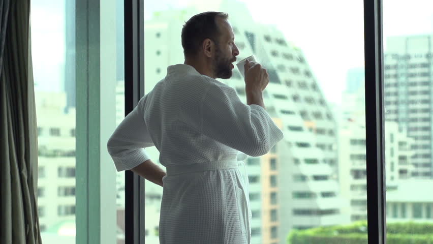 Man walking in hotel's room with coffee and admires view from the window, slow motion shot at 240fps 
