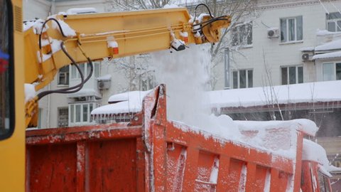 Close-up process of working snow plow. Snow plow loads snow into the truck body. City workers clearing snow from the roads after heavy winter snowfalls.