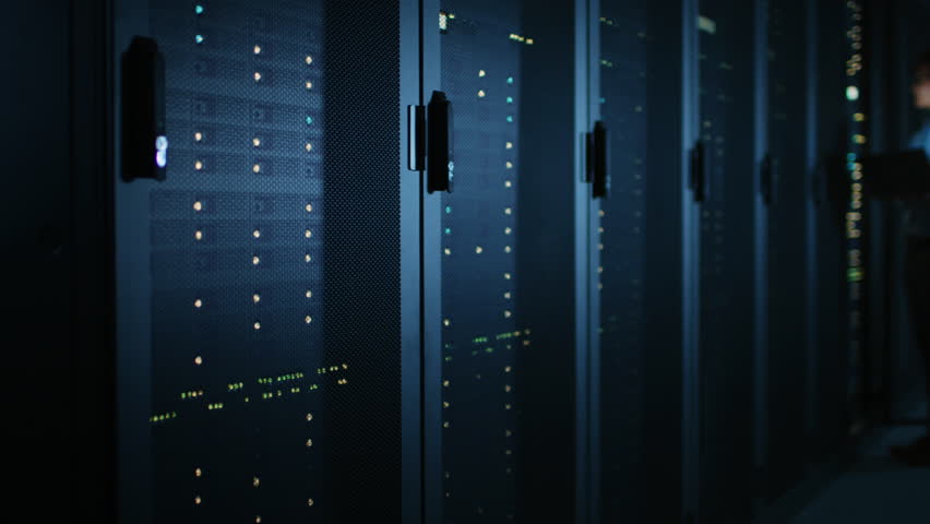 In Dark Data Center: Male IT Specialist Stands Beside the Row of Operational Server Racks, Uses Laptop for Maintenance. Concept for Cloud Computing, Artificial Intelligence, Supercomputer Royalty-Free Stock Footage #1022551672