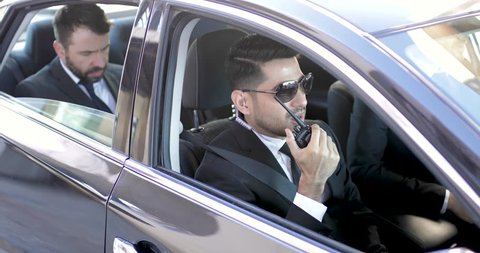 Two bodyguards talking over the radio while transporting an important businessman and providing security