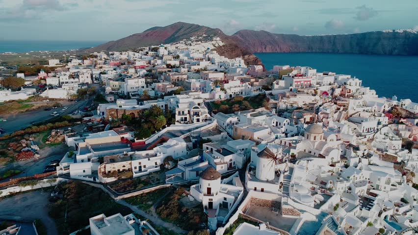 Flying above white houses and famous old castle ruins on Santorini Island, Greece. Village of Oia. Morning sunshine rays.