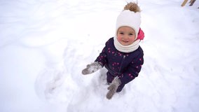 Christmas portrait of cute sweet little girl playing outdoors in winter snowy park. Baby clapping hands cheerfully while looking at camera smiling. Hands in snowy mittens. Slow motion video footage.