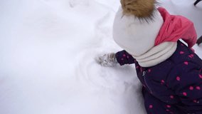 Cute little baby girl trying to draw something in fluffy white snow with hand in mitten. Christmas snowy season. Slow motion full hd video footage.