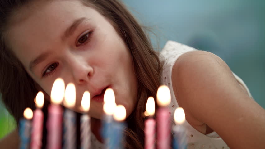 Close up of girl blowing candles on party cake. Portrait of happy child blowing candles in slow motion. Happy birthday wish. Kid birthday celebration tradition