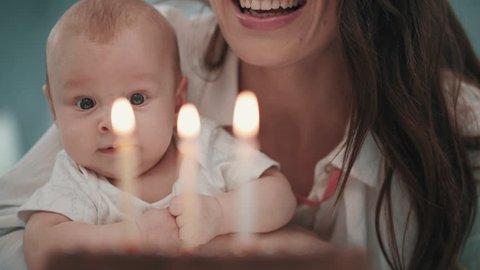 Mom with baby blowing birthday candle in slow motion. Mother with son celebrating happy birthday together. Close up of happy woman with kid blowing candles on cake at family party