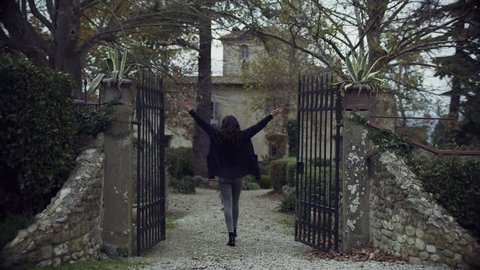 Joyful Italian woman walking up to a gate with a "Sold" sign, throws it away and walks up to her new dream house in Tuscany with soft overcast light. Wide shot on 4k RED camera.