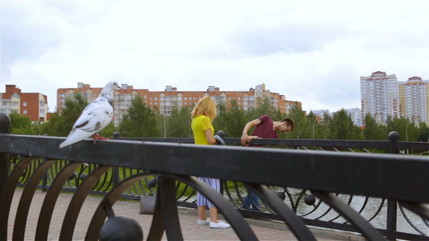 Two teenagers on a bridge in the Park. The guy wants to jump from the bridge in front of his beloved. Young Caucasian heterosexual white couple teenagers find out the relationship. The frightened bird