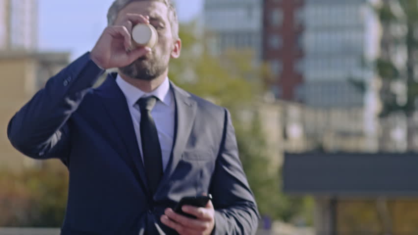 Up-section shot of businessman going through the street, drinking coffee and answering the mobile phone