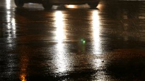 Cars in traffic, headlights in the rain on asphalt, view below. Rain hits the puddles at night. Reflection of car's lights