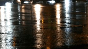 Cars in traffic, headlights in the rain on asphalt, view below. Rain hits the puddles at night. Reflection of car's lights