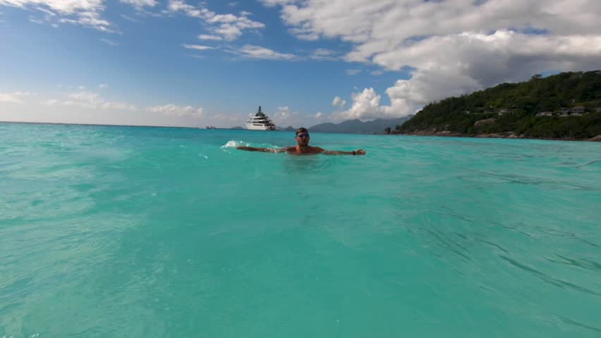 A young man dives in the Indian Ocean. Nearby is a white yacht and the sun is shining. Seychelles, Mahe island. Anse petite. Hotel four seasons.