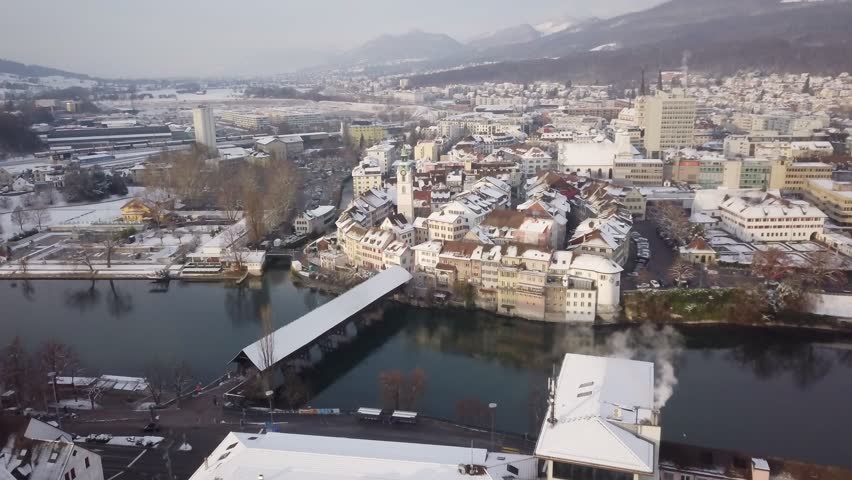 Swiss City Olten during Winter old wooden bridge, medieval tower with fresh snow on rooftops 4k aerial view