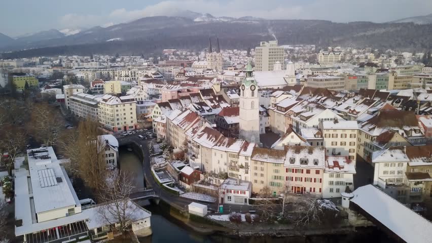 Swiss City Olten during Winter old wooden bridge, medieval tower with fresh snow on rooftops 4k aerial view