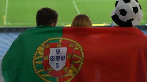 Football fans with Portuguese flag jumping and watching game at stadium, slow-mo
