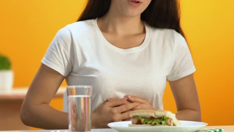 Well fed woman breathing hardly after fast food lunch, taking digestion pill
